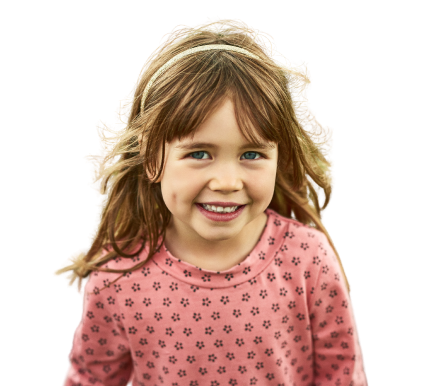 Young girl with long brown hair wearing a pink shirt with small flower patterns, smiling at the camera against a plain background.